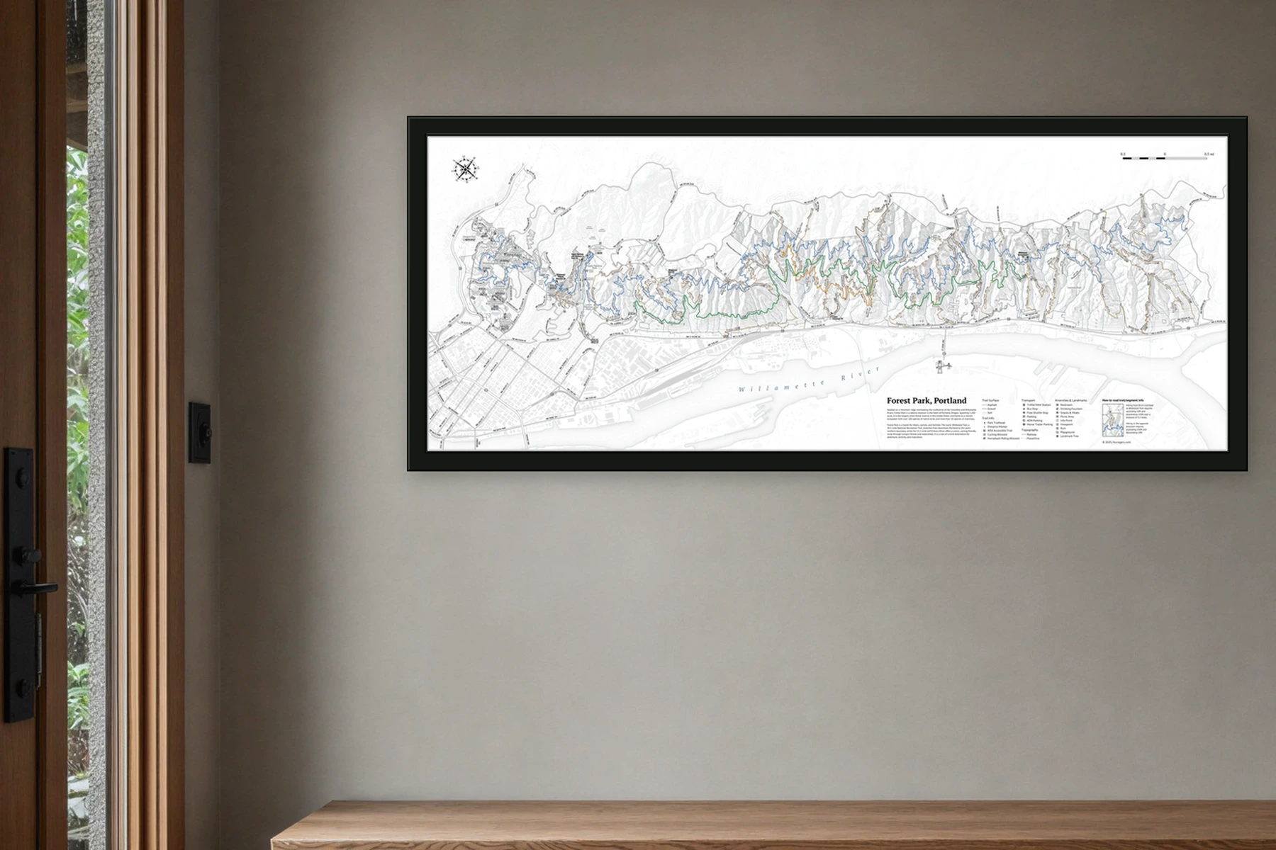 Forest Park wall map in a slim dark frame above an entry bench, with wet greenery visible through the doorway